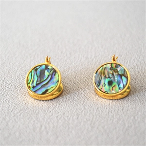 Détail macro de boucles d'oreilles rondes plaquées or avec incrustation d'abalone irisée