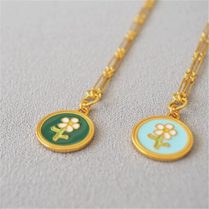 Gros plan détaillé des pendentifs fleur en émail fait main sur chaînes trombones dorées