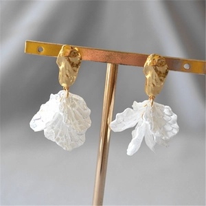 Detail of elegant gold ear studs with white layered fabric petal pendants on a stand
