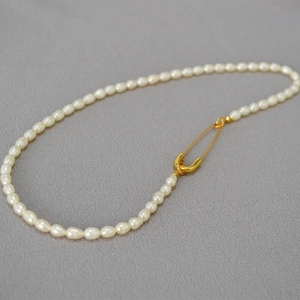 Freshwater rice pearl necklace with a creative gold safety pin clasp on grey fabric