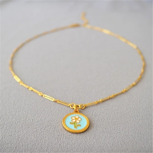 Collier doré vintage avec pendentif fleur en émail bleu clair sur tissu gris texturé