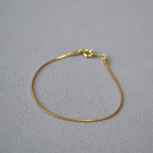 Macro shot of minimalist gold faceted snake chain bracelet with delicate lobster clasp detail