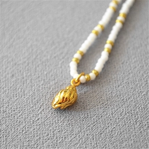 Macro shot of gold-plated seashell pendant with delicate white and gold beads