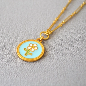 Détail d'un collier doré avec pendentif en émail bleu orné d'une fleur blanche