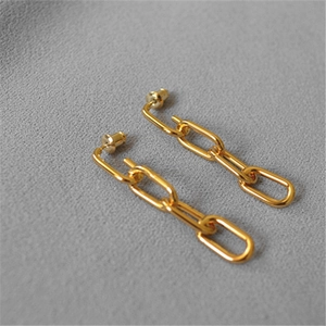 Close-up of golden geometric chain link drop earrings on grey velvet background
