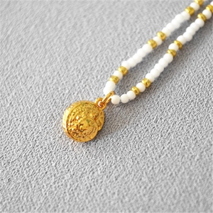 Macro shot of gold hammered round pendant necklace with white and gold beaded chain