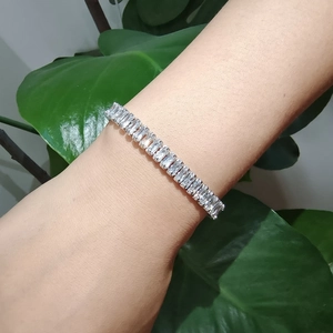Détail d'un bracelet tennis argenté avec zircons taille baguette sur fond naturel vert