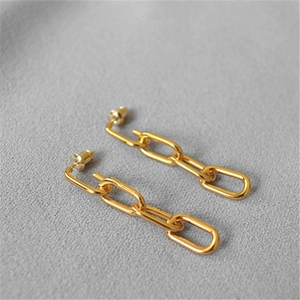 Detailed close-up of golden chain link drop earrings on a grey textured fabric surface