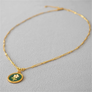 Détail d'une chaîne dorée avec un pendentif floral en émail vert de style rétro