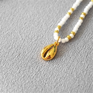 Detailed macro view of gold shell pendant with white beads and polished hardware