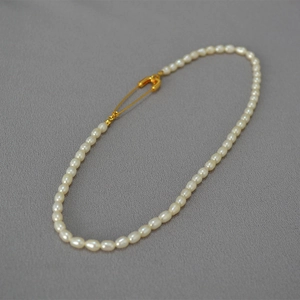 Elegant freshwater pearl necklace with creative golden safety pin clasp on grey fabric