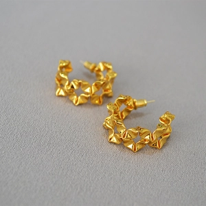 Detailed macro view of gold-plated C-shaped earrings with a modern wrinkled metal texture
