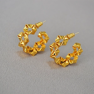 Detailed view of golden pleated C-shaped earrings with 925 silver needles on grey fabric