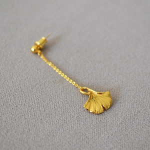 Elegant gold ginkgo leaf dangle earrings with long chains on a grey fabric background