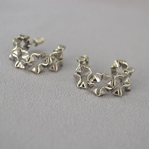Macro view of C-shaped silver earrings with unique origami-style folding flower patterns