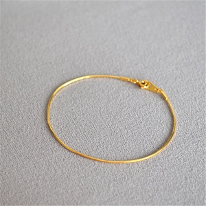 Macro detail of minimalist gold-plated snake chain bracelet with spring ring clasp