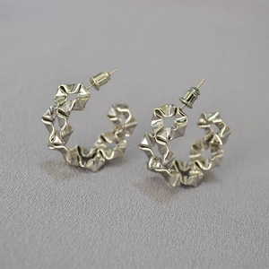 Macro shot of silver C-hoop earrings featuring irregular wavy pleats and polished metal