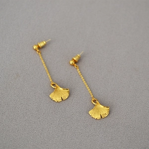 Close-up of gold ginkgo leaf earrings with long chain dangles on gray texture