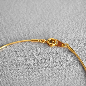 Detail of a thin gold-plated snake chain with a spring ring clasp on grey fabric