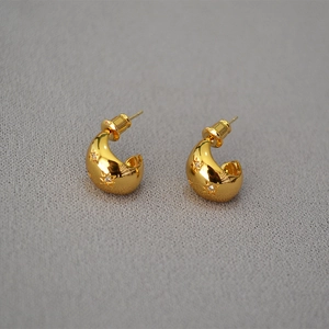 Close-up of golden C-shaped hoop earrings with star engravings and inlaid zircons