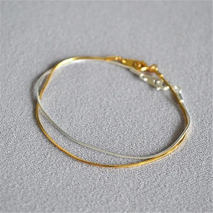 Detailed close-up of delicate gold and silver snake chain bracelet with lobster clasp