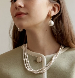 Detail of elegant three-layer pearl necklace and large pearl drop earrings on a model