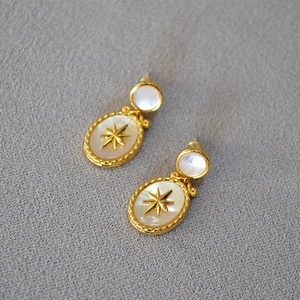 Macro shot of retro gold drop earrings with white mother-of-pearl and star relief details