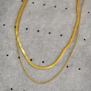 Detail of double-layer gold snake chain and cable link necklace on grey velvet surface