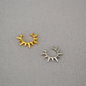 Detailed view of punk style silver and gold spiked ear cuffs on a grey background