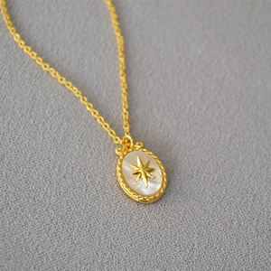 Golden North Star necklace with white mother of pearl oval pendant on grey fabric