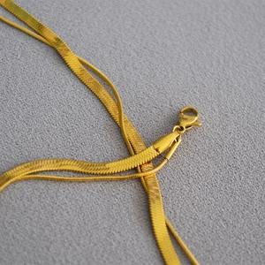 Detail of gold double-layered snake chain necklace with lobster clasp on grey fabric