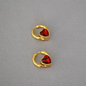 Détail de boucles d'oreilles en laiton doré avec pierres en verre rouge en forme de cœur