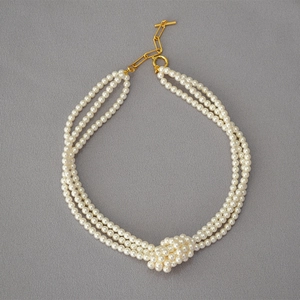 Detailed view of triple-strand glass pearl necklace with knot accent and golden toggle clasp