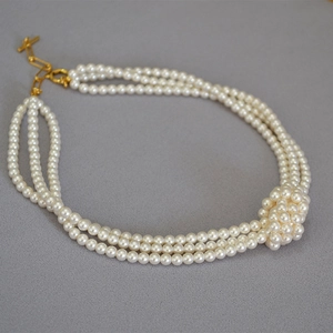 Close-up of triple-layer pearl necklace with golden OT clasp and woven pearl knot detail