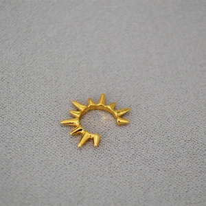 Macro shot of gold spike cuff earring with a radiant punk-style rivet design on gray fabric