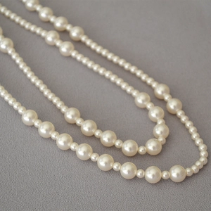 Macro shot of tiered pearl necklace with alternating sizes on textured grey fabric
