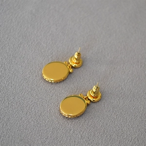 Elegant gold oval pendant earrings with beaded edge and North Star design on gray texture
