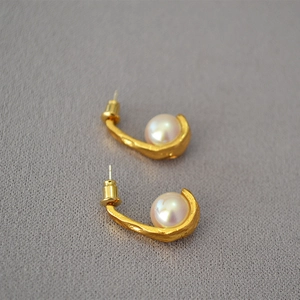 Macro detail of matte gold textured hook earrings with elegant inlaid white pearls