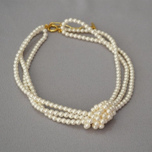 Detailed view of elegant triple-layer glass pearl necklace with decorative center knot