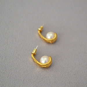 Detailed close-up of vintage matte gold hook earrings featuring round white pearls