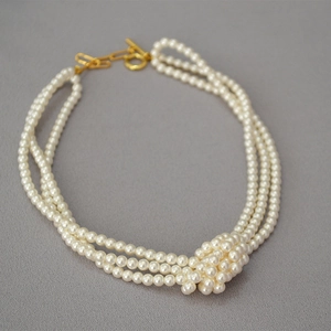 Detail of multi-strand layered pearl necklace featuring an elegant knotted design and golden OT clasp