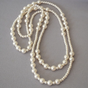 Detail of multi-layered long pearl necklace with alternating size round beads on grey fabric