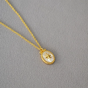Macro detail of gold oval necklace featuring a North Star on white mother of pearl