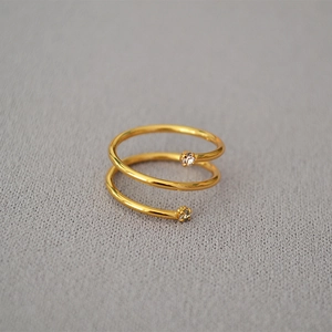 Dettaglio di un anello a spirale a doppio strato dorato con accenti di zirconi lucidi