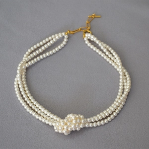 Close-up of triple-layered glass pearl necklace with woven knot and golden OT clasp