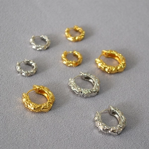 Detailed texture of gold and silver irregular lava style hoop earrings on grey background