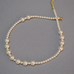 Collier de perles élégant avec tailles alternées et fermoir doré sur tissu gris