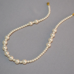 Vue détaillée du collier de perles dégradées avec fermoir doré sur tissu gris texturé