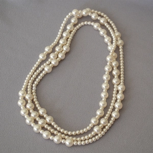 Detail of three-layer faux pearl necklace featuring gradient beads on grey fabric