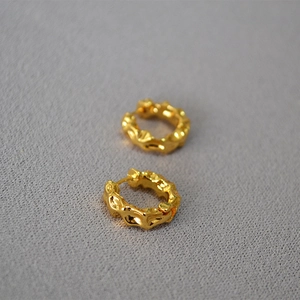 Detailed view of gold irregular lava texture hoop earrings on grey textured fabric